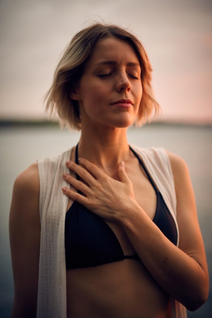 Photo by Darius Bashar woman in white vest and black bikini with hand on chest
