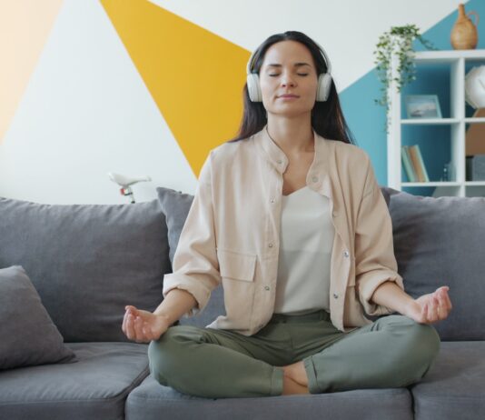 집에서 즐기는 ‘마음 챙김 스트레칭’, 일상에 활력을 더하다 Woman meditating on couch with headphones on